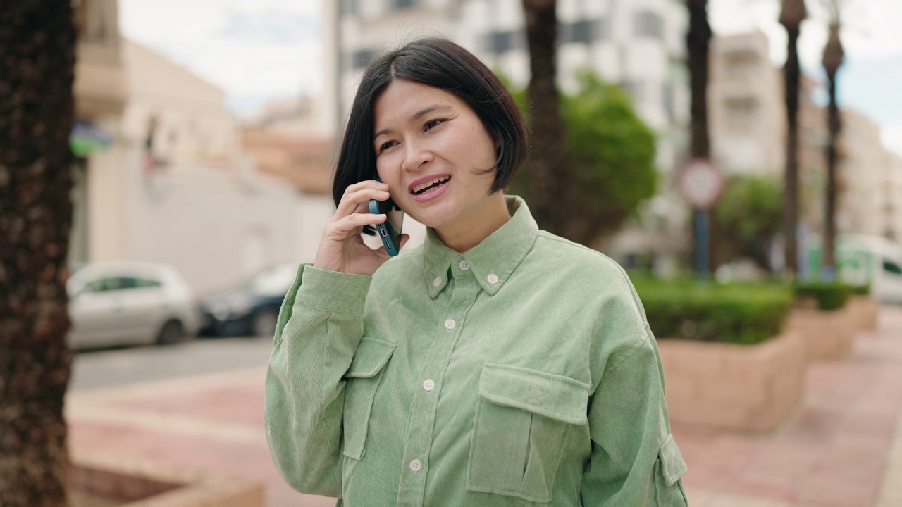 年轻的中国女子微笑着自信地在街上用智能手机聊天视频素材