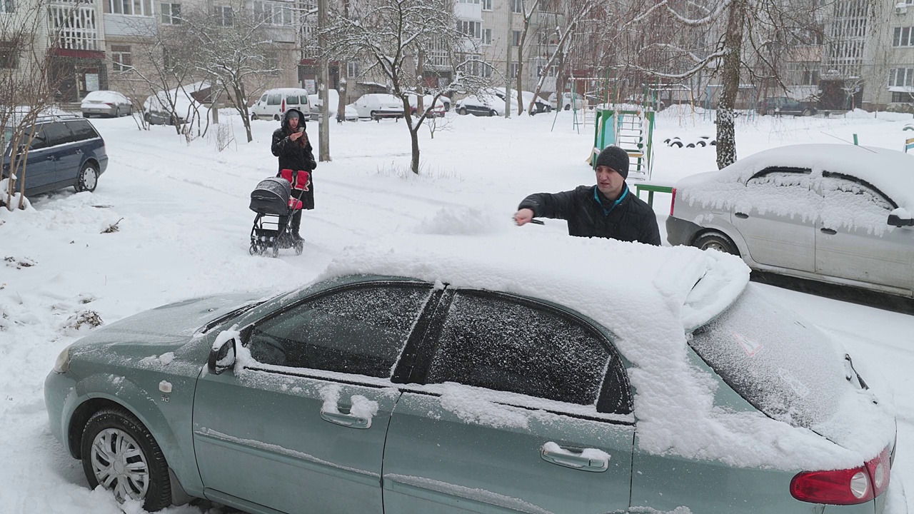 这家人要开车去市里自驾游。爸爸把车上的雪擦干净。视频素材