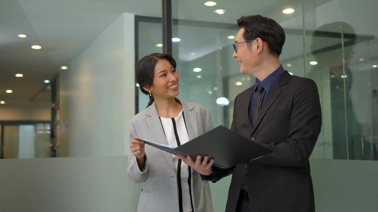 微笑的亚洲女商人在办公室谈话期间向她的经理展示文件报告。秘书和老板在办公室讨论新的战略和业务发展计划。视频下载