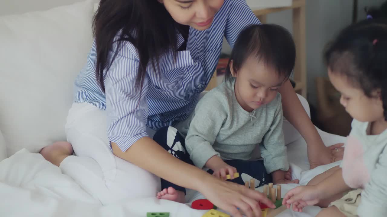 亚洲妈妈和小女孩正在床上学习玩彩色的木制玩具视频素材