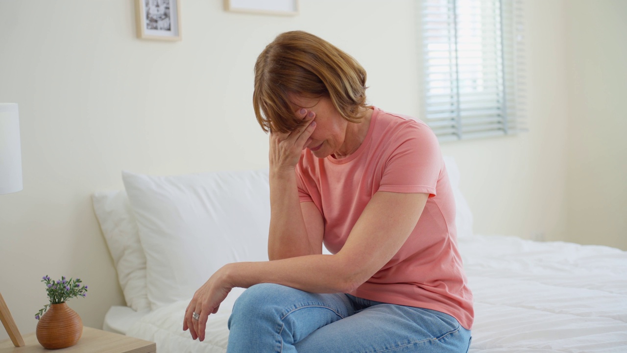 白人老年抑郁妇女独自坐在家里的卧室里。有魅力的老年成熟女性感到悲伤，孤独和沮丧的生活问题，想到金钱债务，预算损失，破产。视频素材