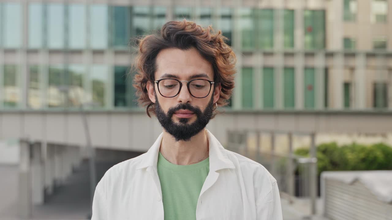 年轻的西班牙男子留着胡子，戴着眼镜，带着快乐的表情看着镜头。人类的情感和感觉视频素材