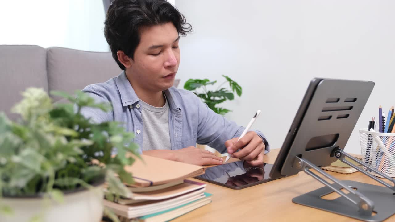 年轻的亚洲男子挣扎着，坐在家里客厅的沙发上摆弄着平板电脑视频素材