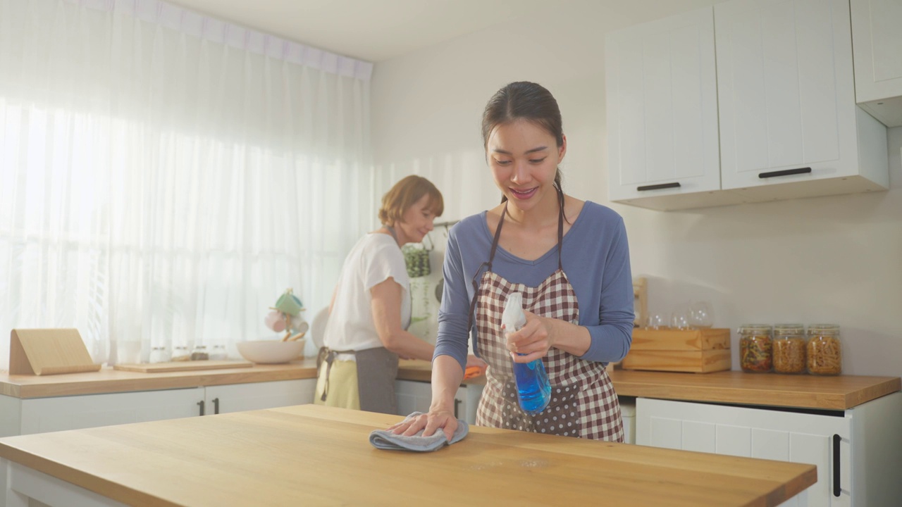 白种人老年妇女和女儿在家里打扫厨房。迷人的女管家和成熟的清洁工系上围裙，在家里做家务或杂务时感到快乐和放松。视频素材