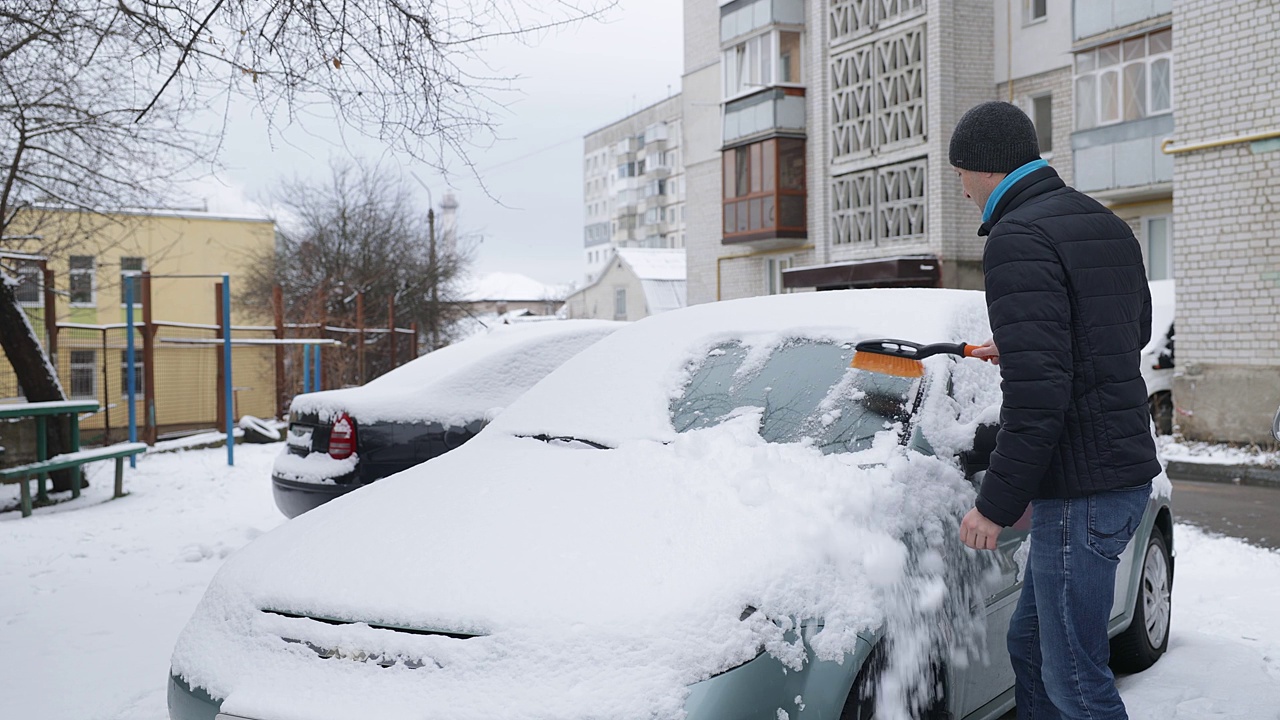 那个男人一边清理汽车上的积雪，一边感到背部疼痛。视频素材