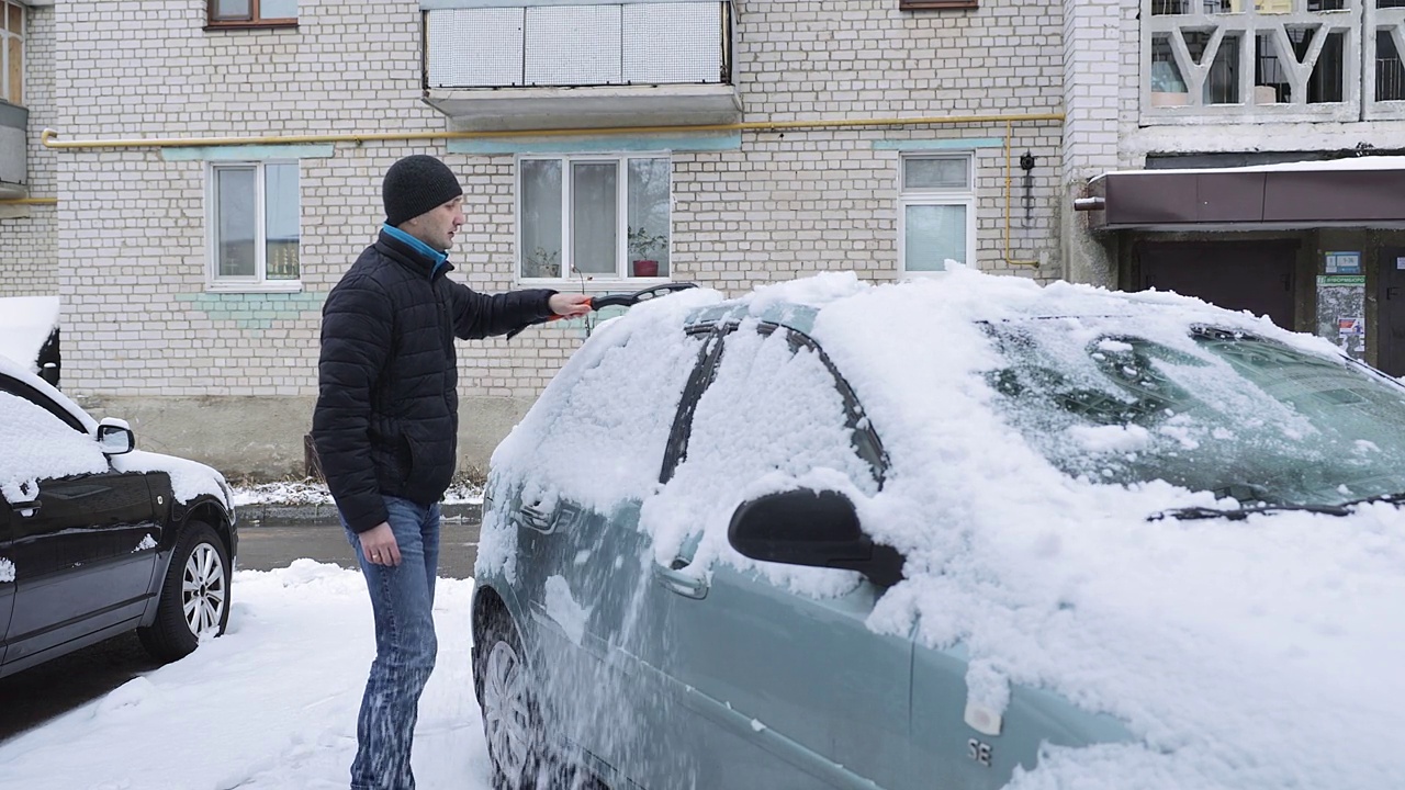 那个男人一边清理汽车上的积雪，一边感到背部疼痛。视频素材