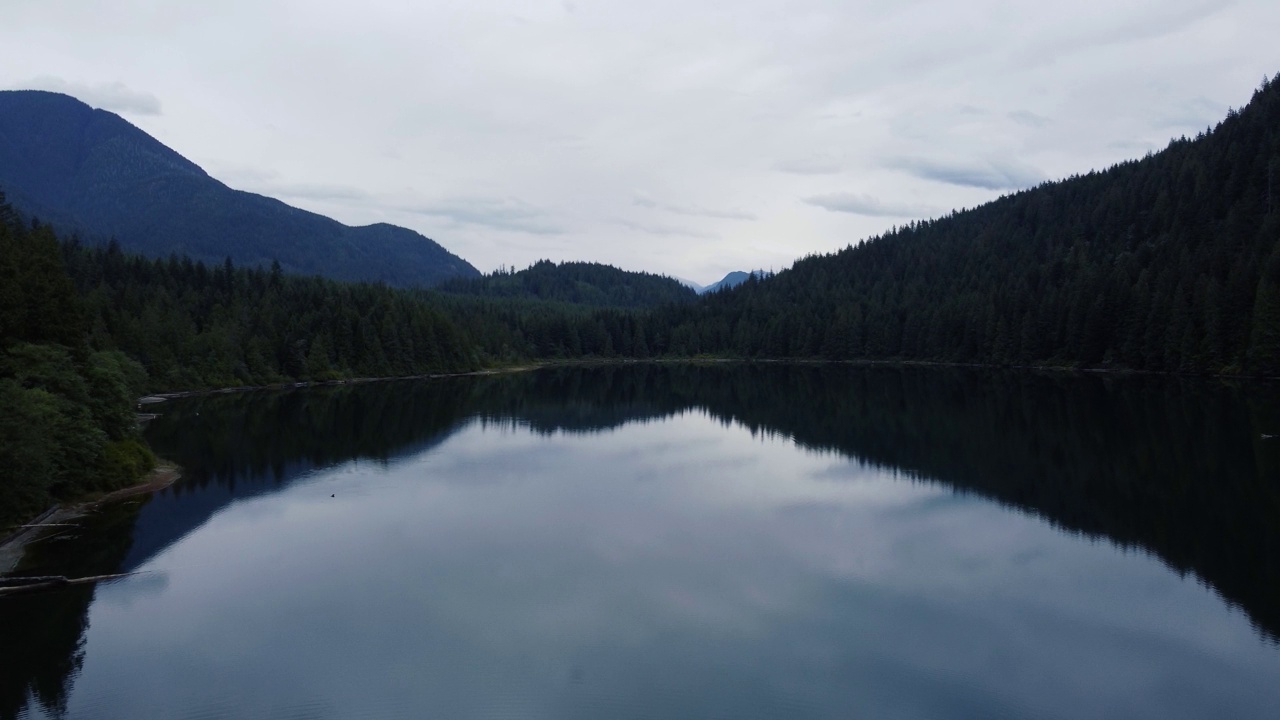 在阴天，鸟瞰水晶般清澈的湖泊周围的森林山丘视频素材