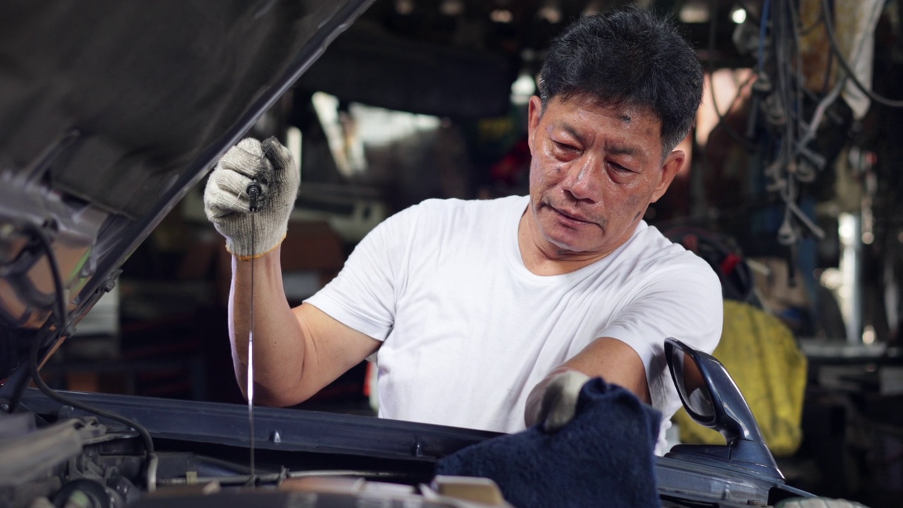 高级亚洲男性汽车修理工工人在汽车服务站检查汽车发动机的油位。汽车维修和汽车服务车库概念。视频素材