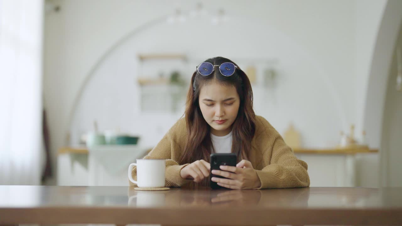 兴奋的亚洲女性正在使用智能手机。年轻的亚洲女人在家里快乐和微笑视频素材