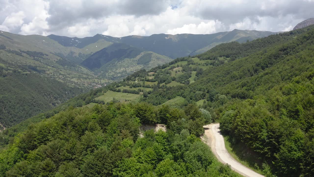 空中摄影车显示汽车行驶在绿色山谷森林环绕的道路上视频素材