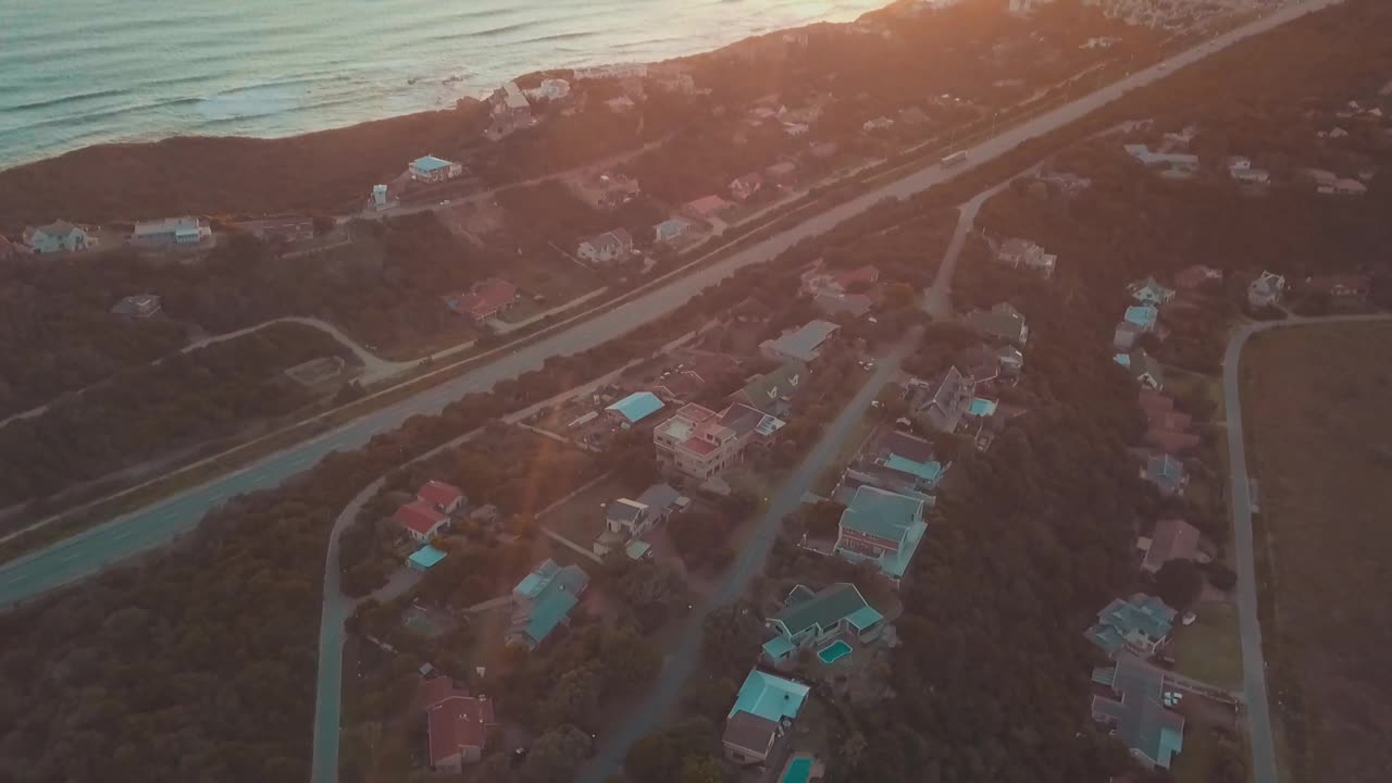 航拍的汽车在海边的建筑物包围的道路上，以4K日落为背景视频素材