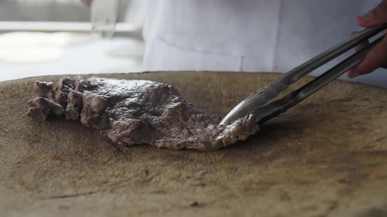 墨西哥马萨特兰的一家露天塔可餐厅里，厨师在质朴的砧板上切Carne Asada牛排视频素材