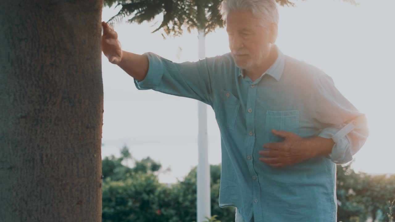 头部特写生病的老人在公园摸他的胸部感觉很糟糕。疲惫的成熟男性在树旁休息。视频素材