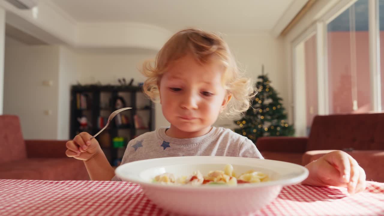 孩子在厨房的桌子上吃通心粉加番茄酱。妈妈给孩子加了番茄酱。不良饮食习惯视频素材