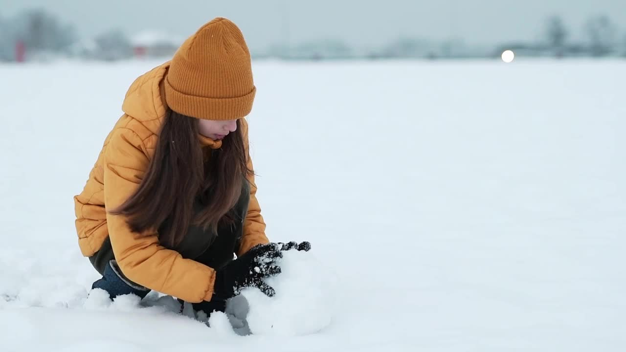 一个快乐的少年享受着雪。女孩在街上堆雪人视频素材