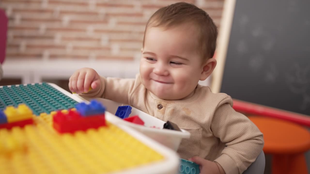 可爱的幼儿拿着塑料积木坐在幼儿园的桌子上视频素材画面1