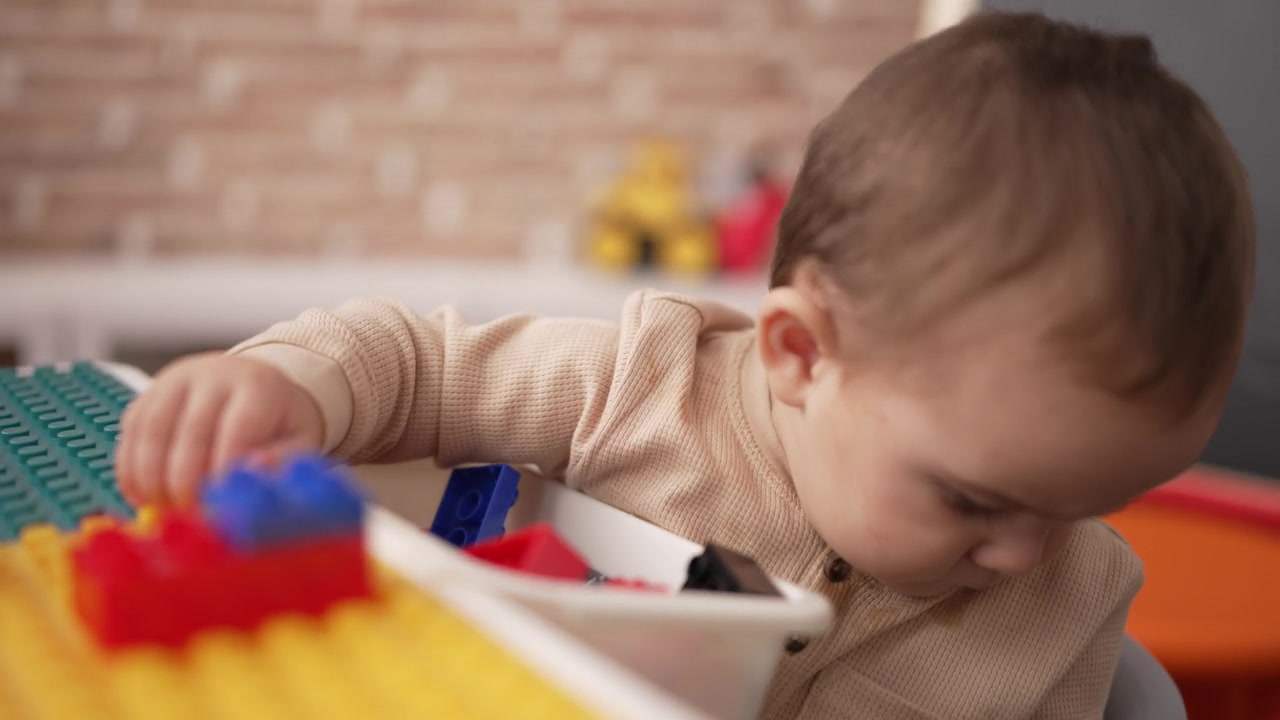 可爱的幼儿拿着塑料积木坐在幼儿园的桌子上视频素材画面2