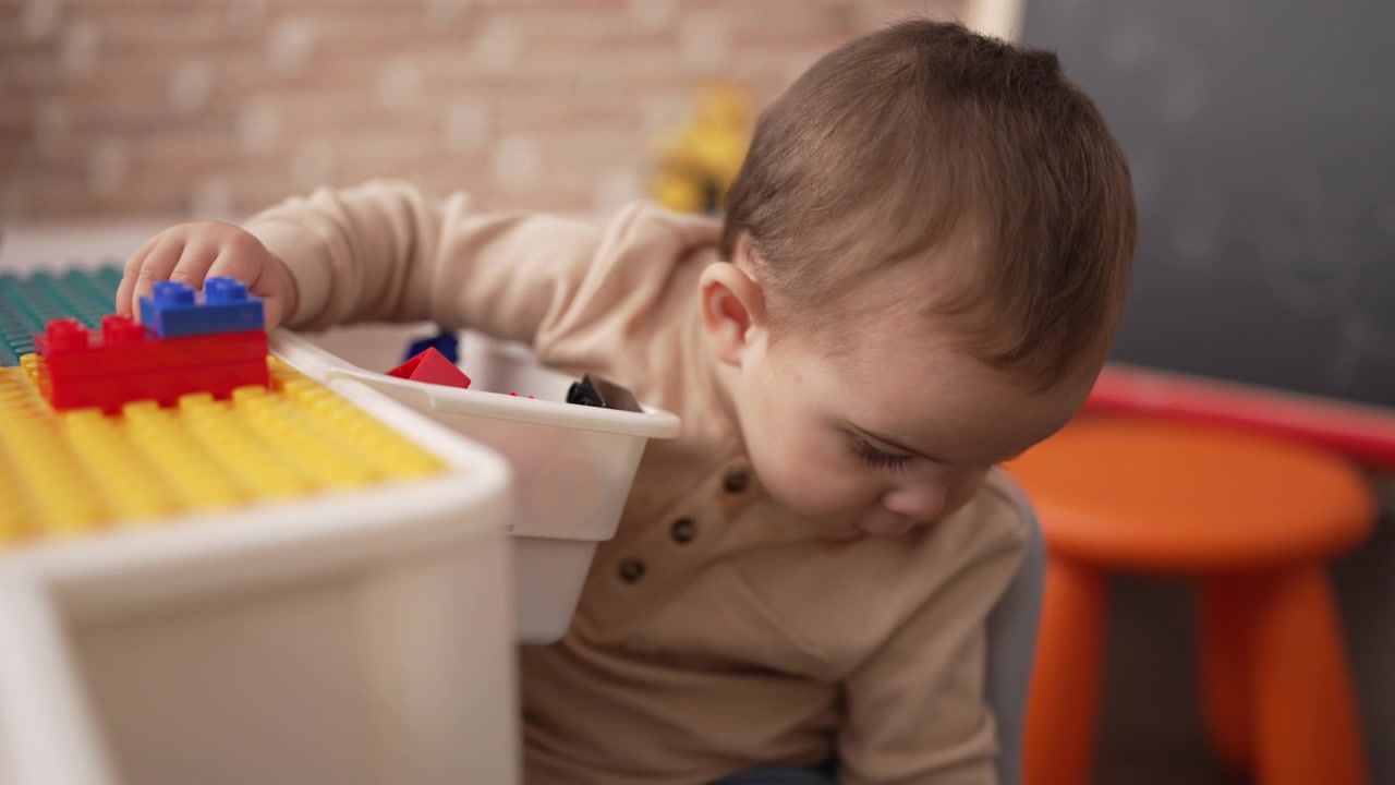 可爱的幼儿拿着塑料积木坐在幼儿园的桌子上视频素材画面3