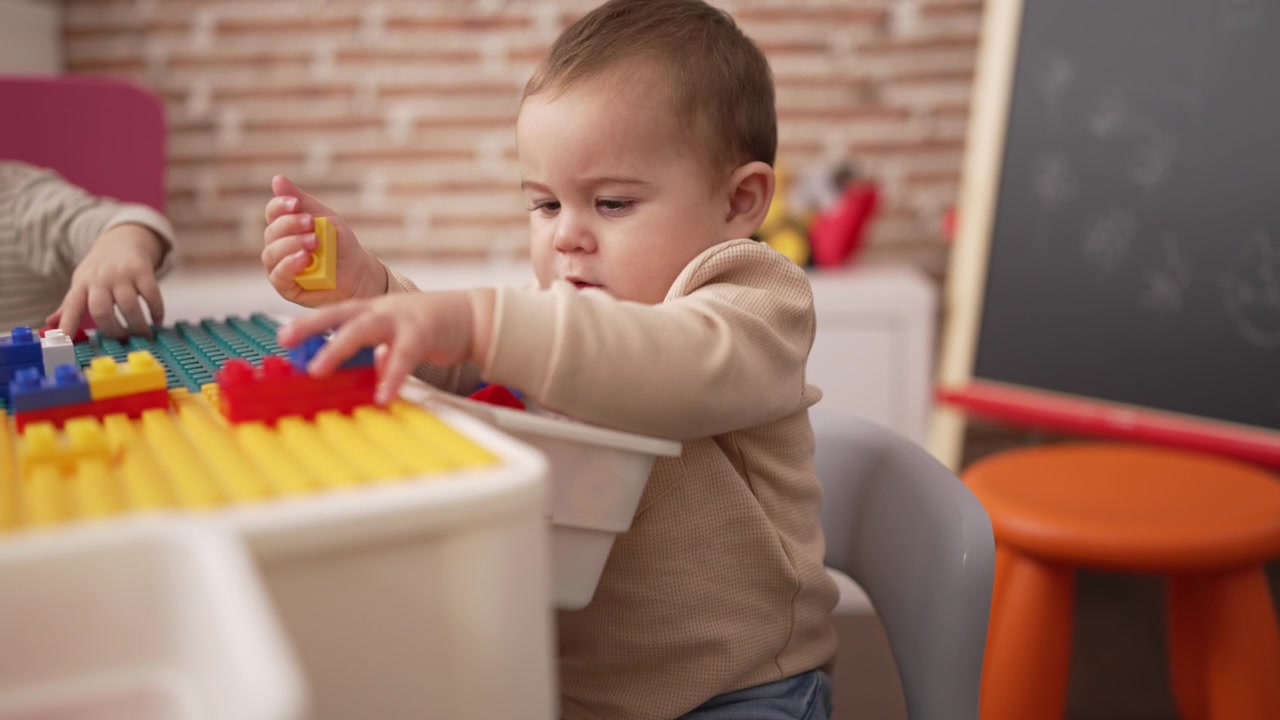 可爱的幼儿拿着塑料积木坐在幼儿园的桌子上视频素材画面4