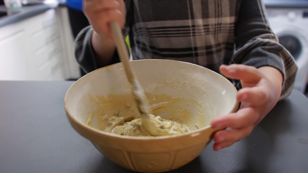 一个女孩在厨房里用木勺在碗里搅拌饼干面团蛋糕混合物视频素材