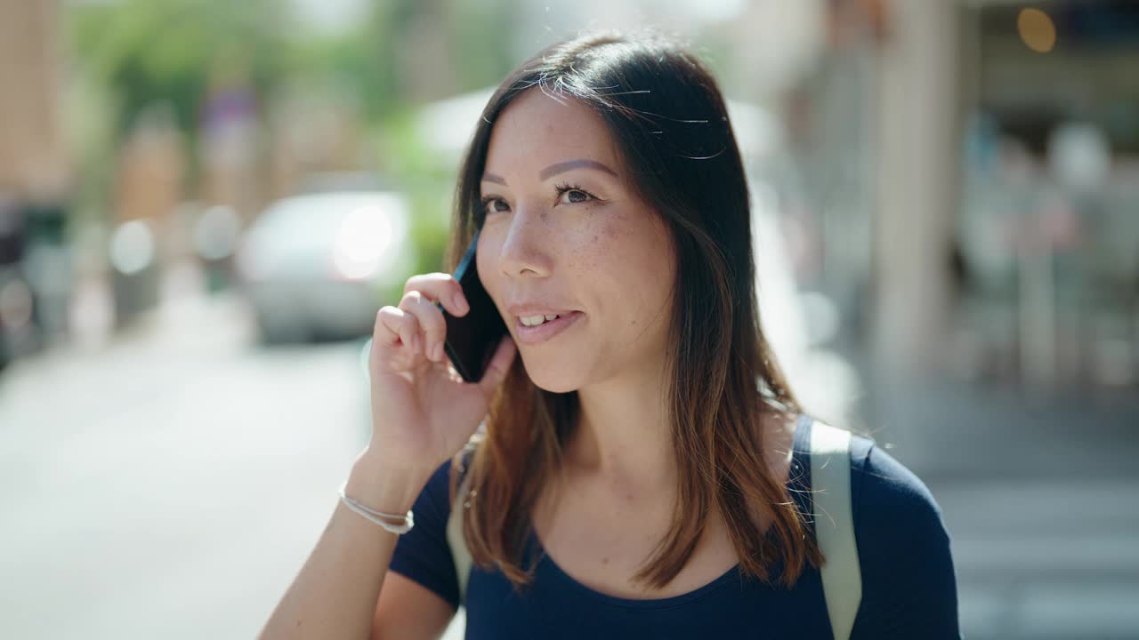 年轻的亚洲女子微笑着自信地在街上用智能手机说话视频素材