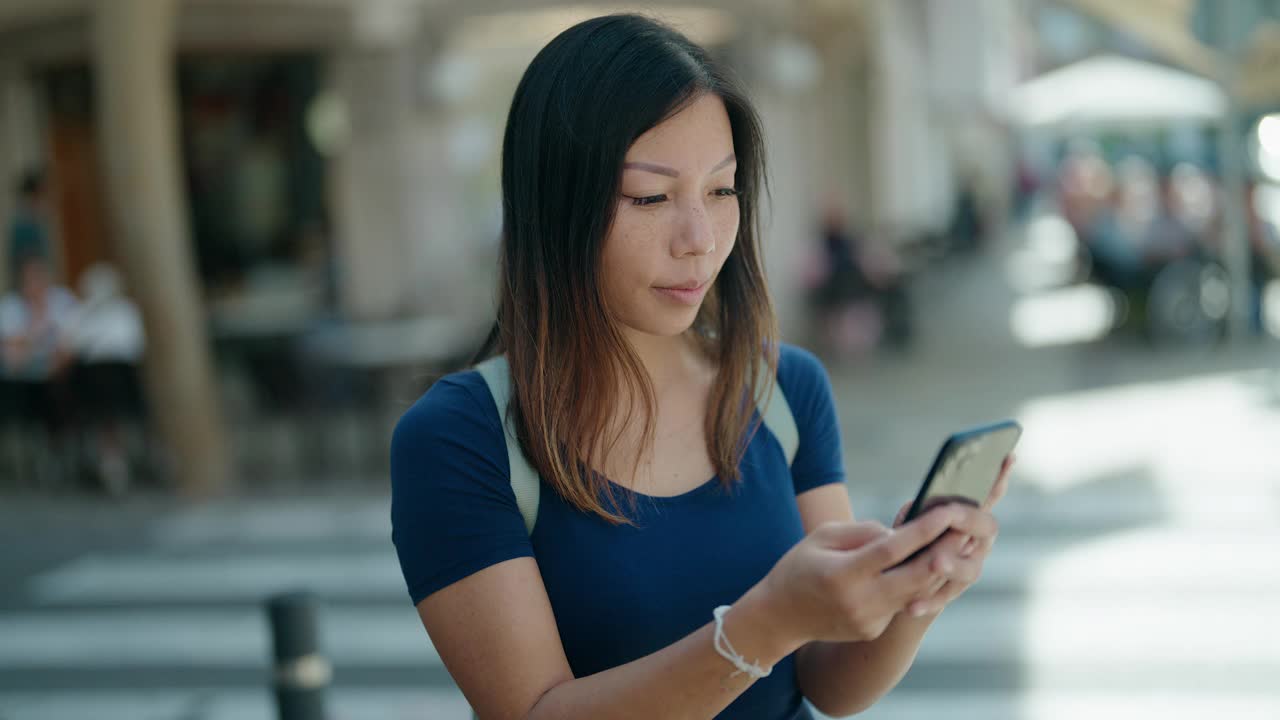 年轻的亚洲女子在咖啡店露台使用智能手机微笑自信视频素材