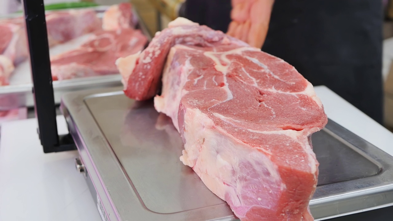 肉铺里的屠夫拿着电子秤上的红牛肉生排，称重后切好卖给顾客。从农场零售有机肉类视频素材