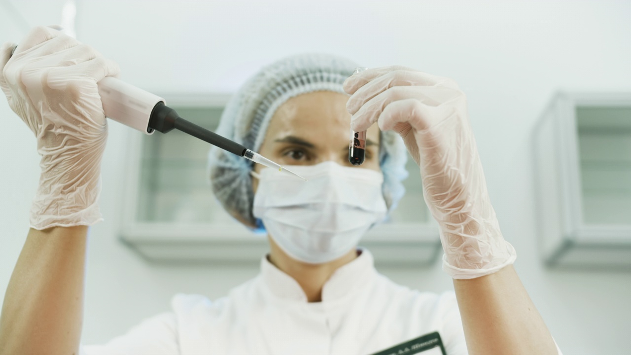一个戴着口罩的女科学家的真实肖像，用微量吸管进行分析。视频素材