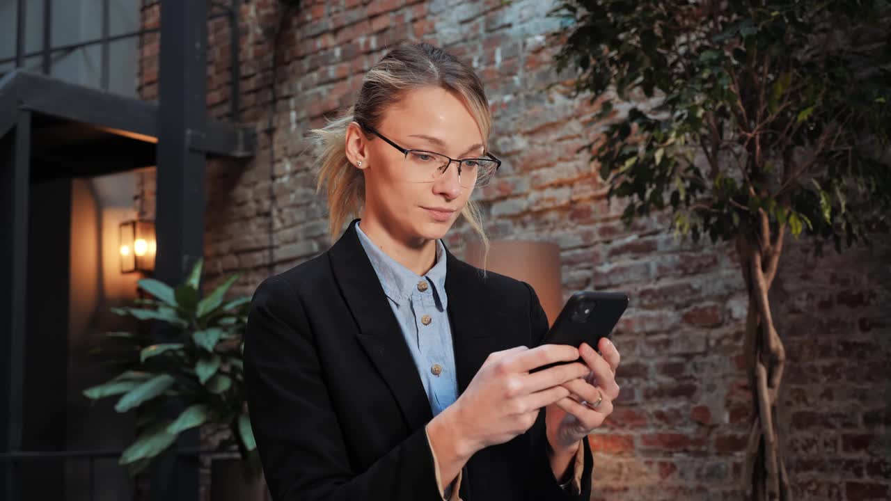 近距离观看漂亮的年轻女商人使用手机和微笑在现代办公室。在社交媒体上发短信，分享信息，回复电子邮件，享受快乐的移动技术。视频素材