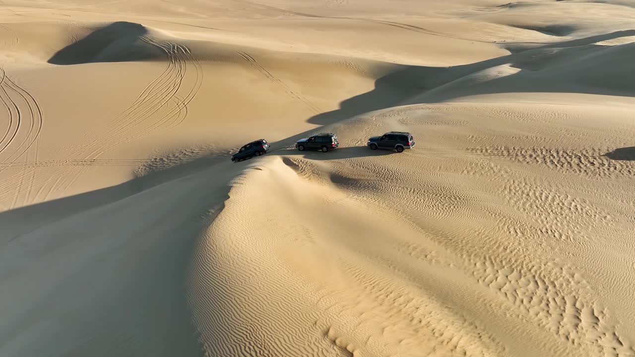 在埃及的撒哈拉沙漠，一支由4x4旅游车组成的车队正沿着沙丘向下行驶。视频素材