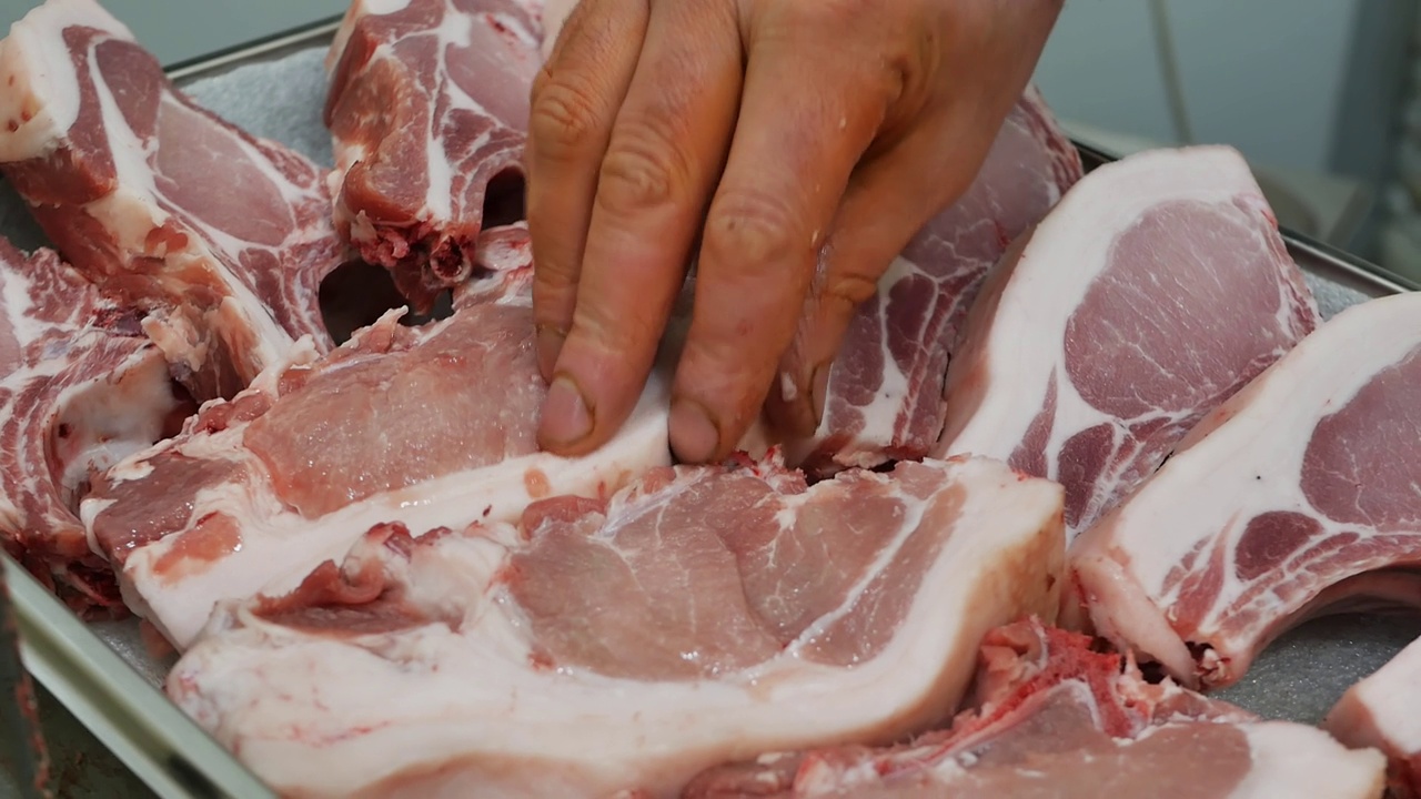 肉铺里卖肉的手的特写，他把生肉和猪内脏放在有机农村产品零售的橱窗上。视频素材