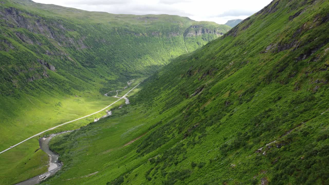 Kvassdalen郁郁葱葱的原始山谷通往挪威Vikafjell附近的Myrkdalen -空中跟随绿色山坡向下，同时看着阳光照射在底部的河流和道路上视频素材