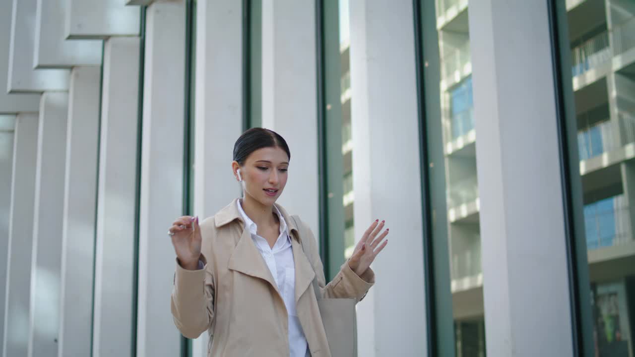 戴着耳机打电话的女子走在城市街道上。女士讲话视频素材