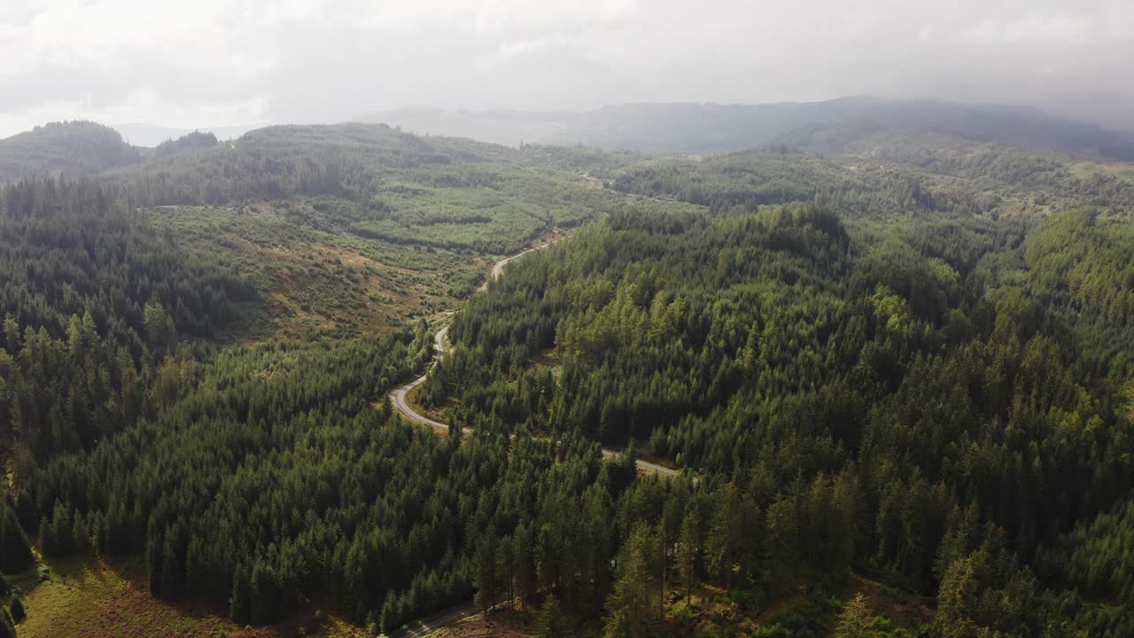 当一辆汽车行驶在乡村道路上时，一架无人机在苏格兰巨大的森林上空拍摄到令人难以置信的光线。视频素材