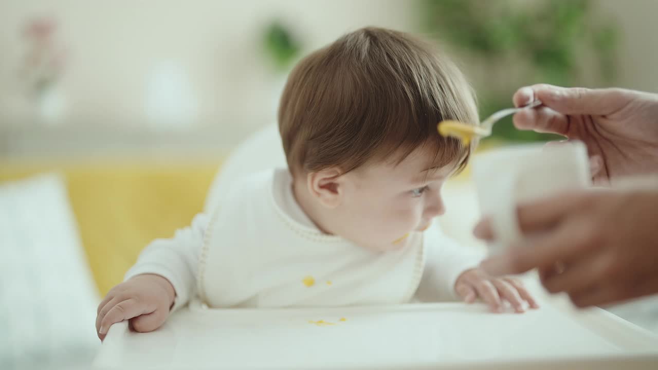 可爱的西班牙幼儿坐在家里的高脚椅上吃东西视频素材