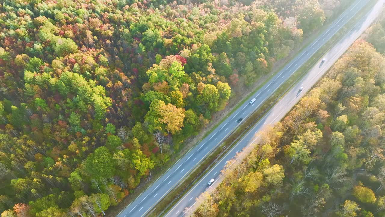 鸟瞰繁忙的美国高速公路与快速移动的交通包围的秋天森林树木。州际运输概念视频素材