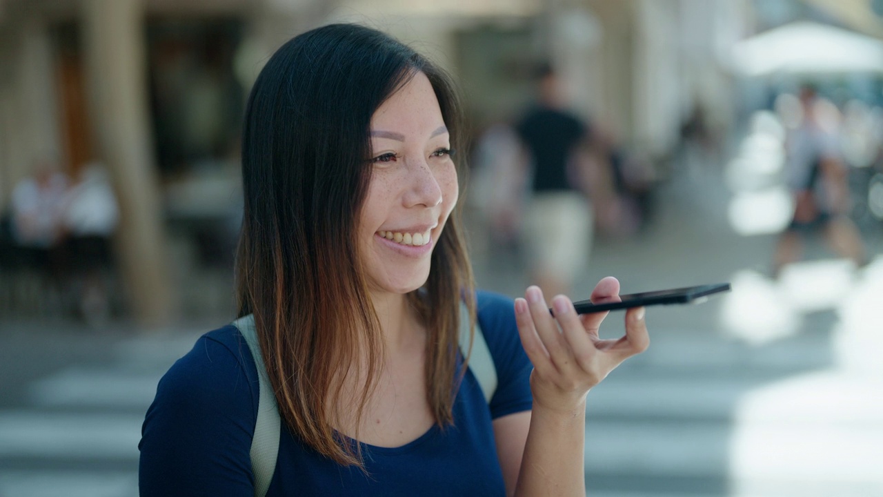 年轻的亚洲女子微笑着自信地在咖啡馆露台上用智能手机说话视频素材