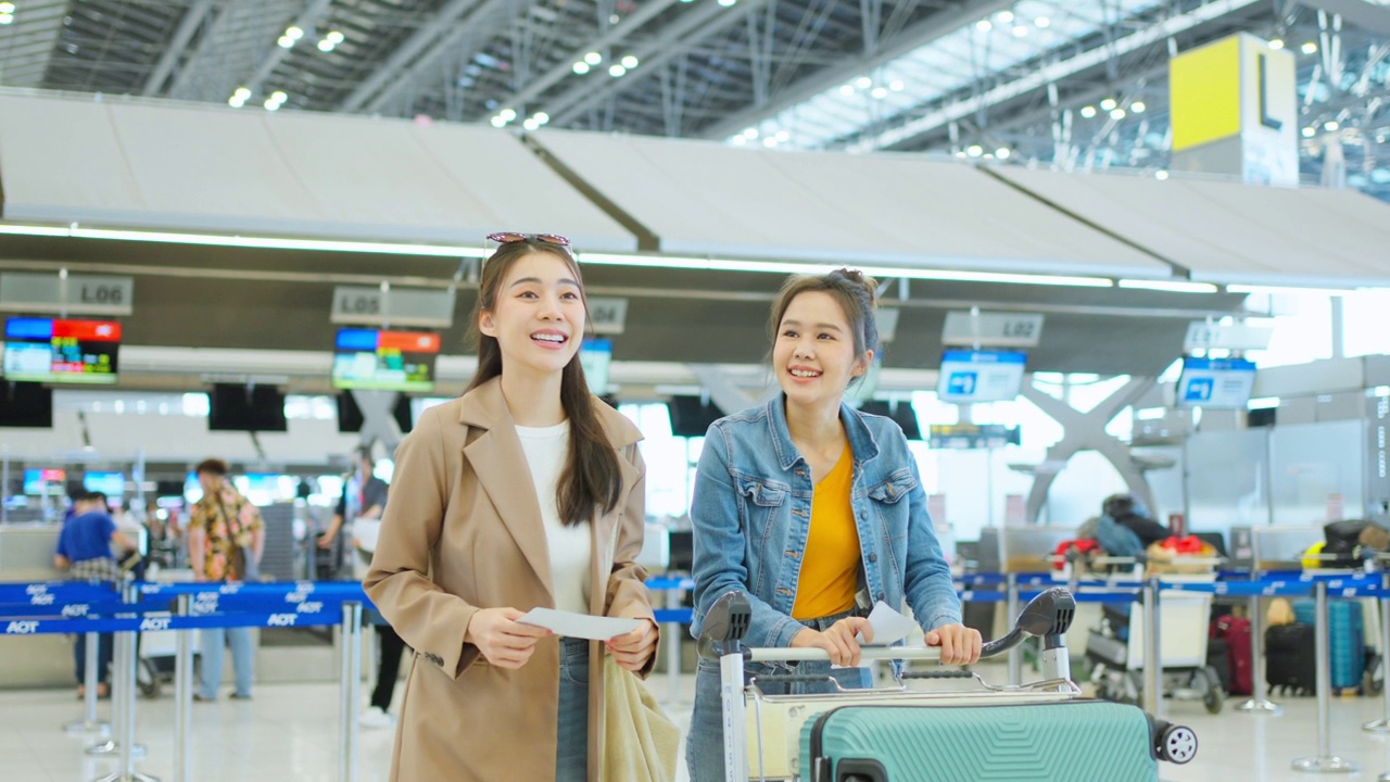 亚洲年轻女性乘客在机场航站楼走向登机门。迷人美丽的女游客朋友心情愉快，兴奋地乘飞机出国旅游度假旅行。视频素材