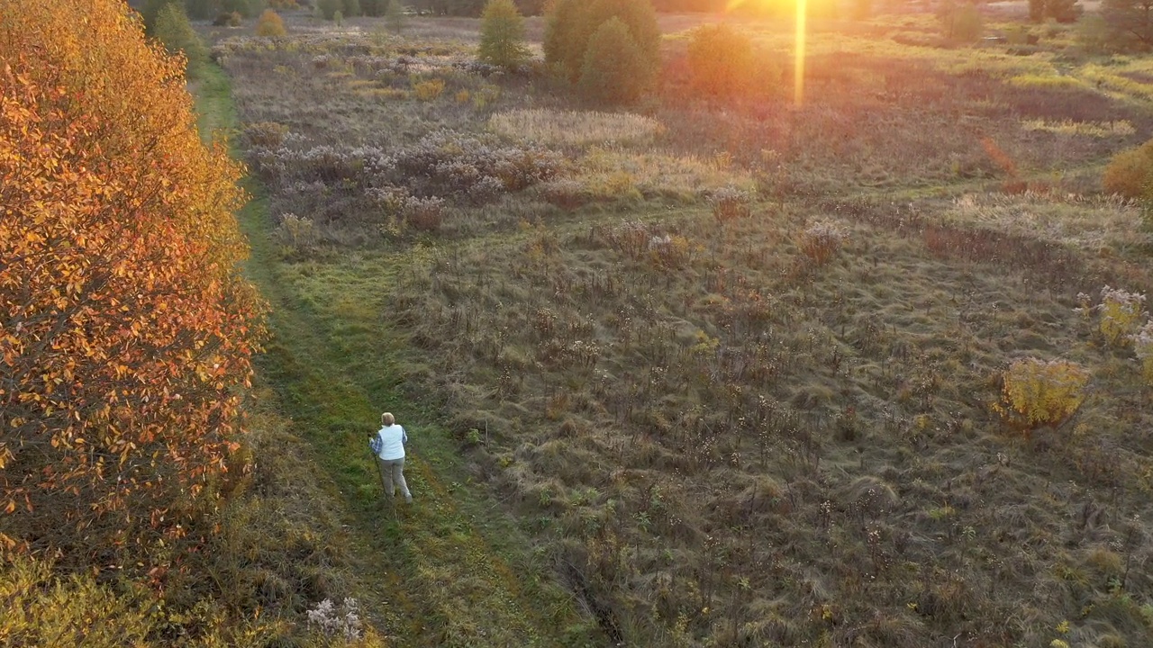 带着登山杆的老妇人走在夕阳下的乡村道路上视频素材