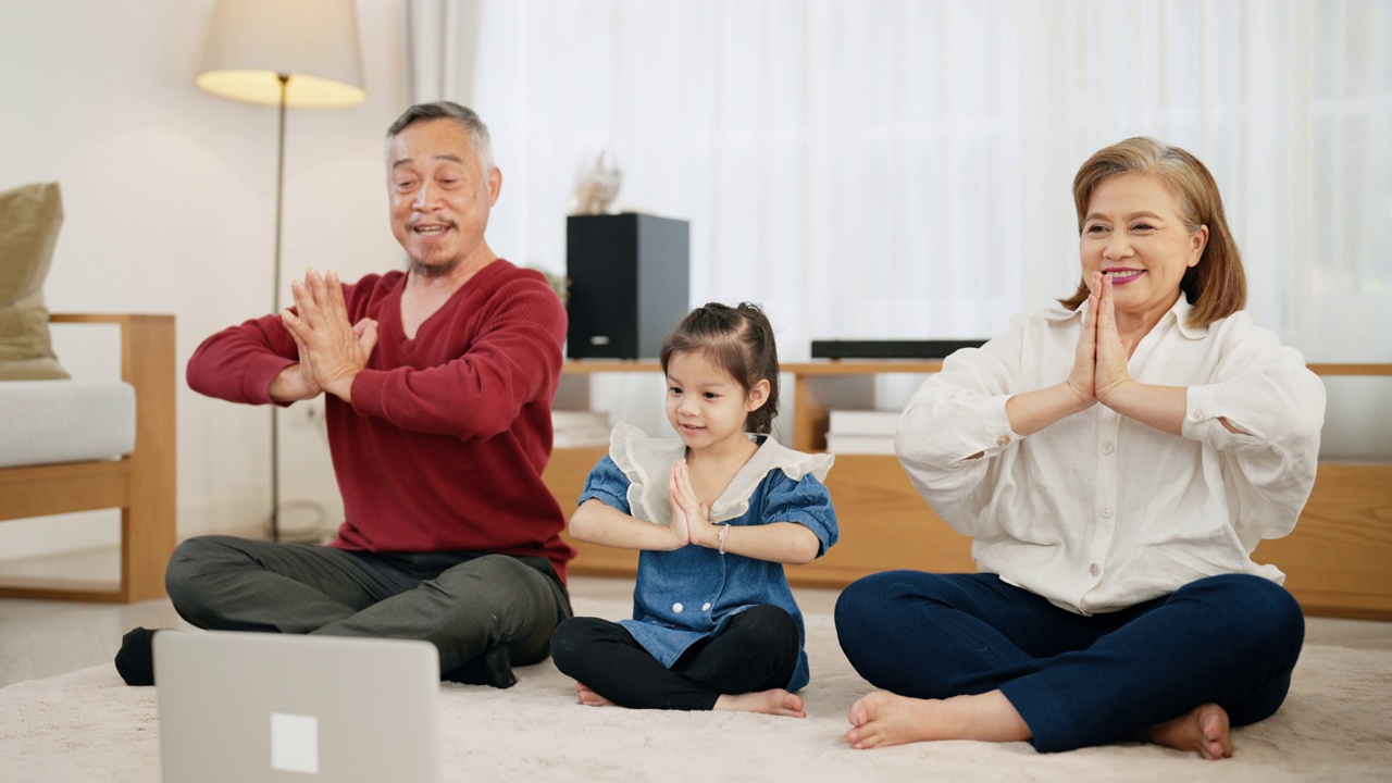 图为，亚洲老人和女孙辈正在用笔记本电脑观看网络视频进行冥想。视频素材