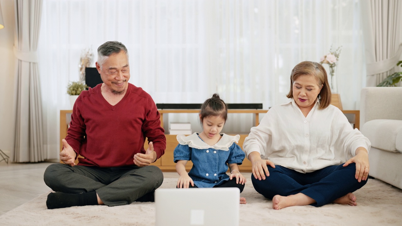 图为，亚洲老人和女孙辈正在用笔记本电脑观看网络视频进行冥想。视频素材