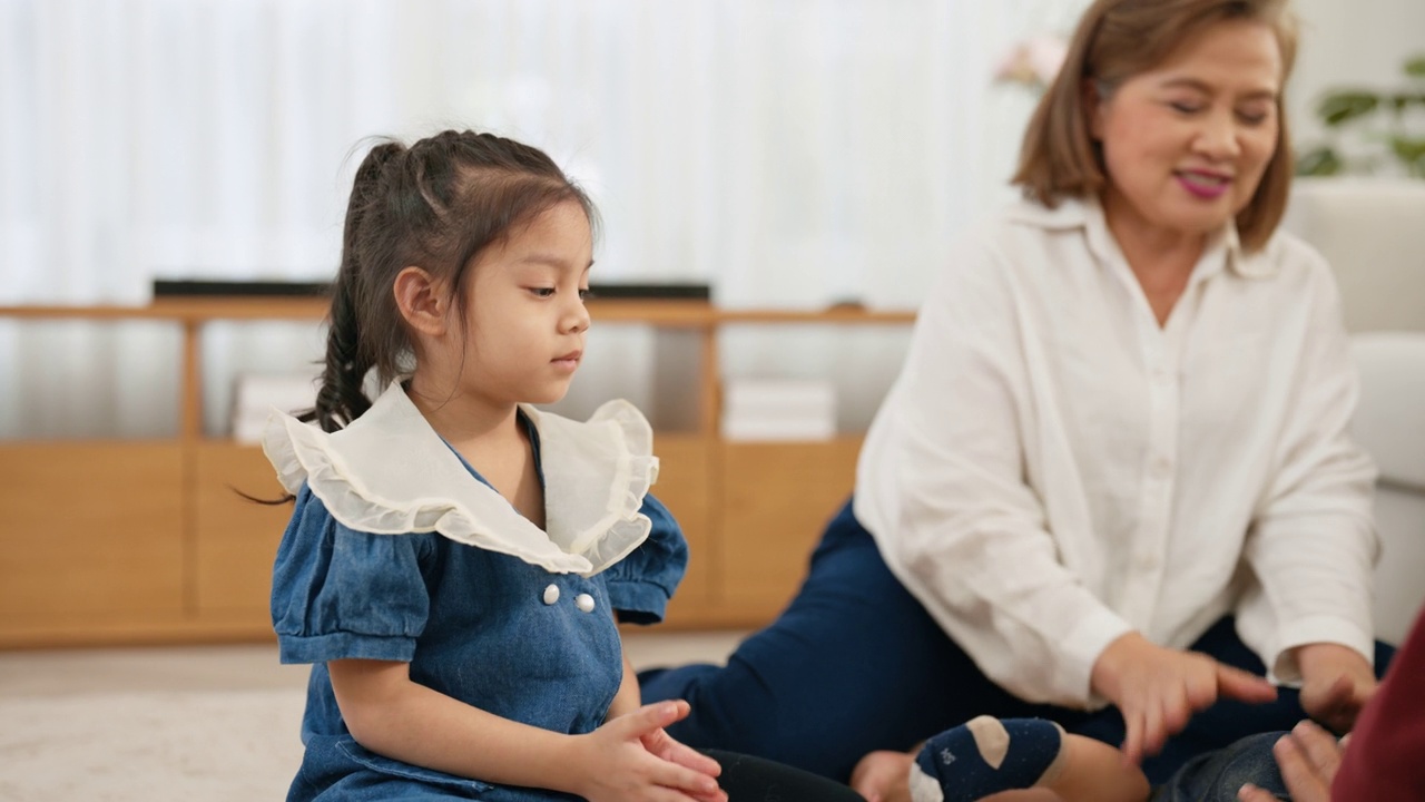 一个亚洲女孙子和她的祖母坐在客厅的地板上，鼓掌鼓励婴儿。视频素材