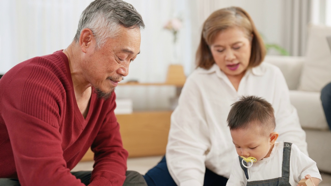 亚洲老年祖父母和他们的孙子坐在地板上，玩木制玩具积木来增强想象力。视频素材