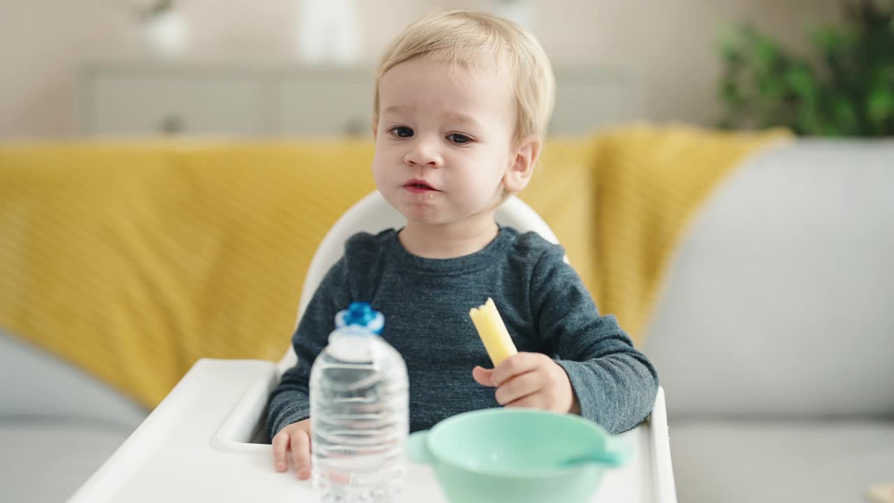 可爱的金发小孩坐在高脚椅上在家吃零食视频素材