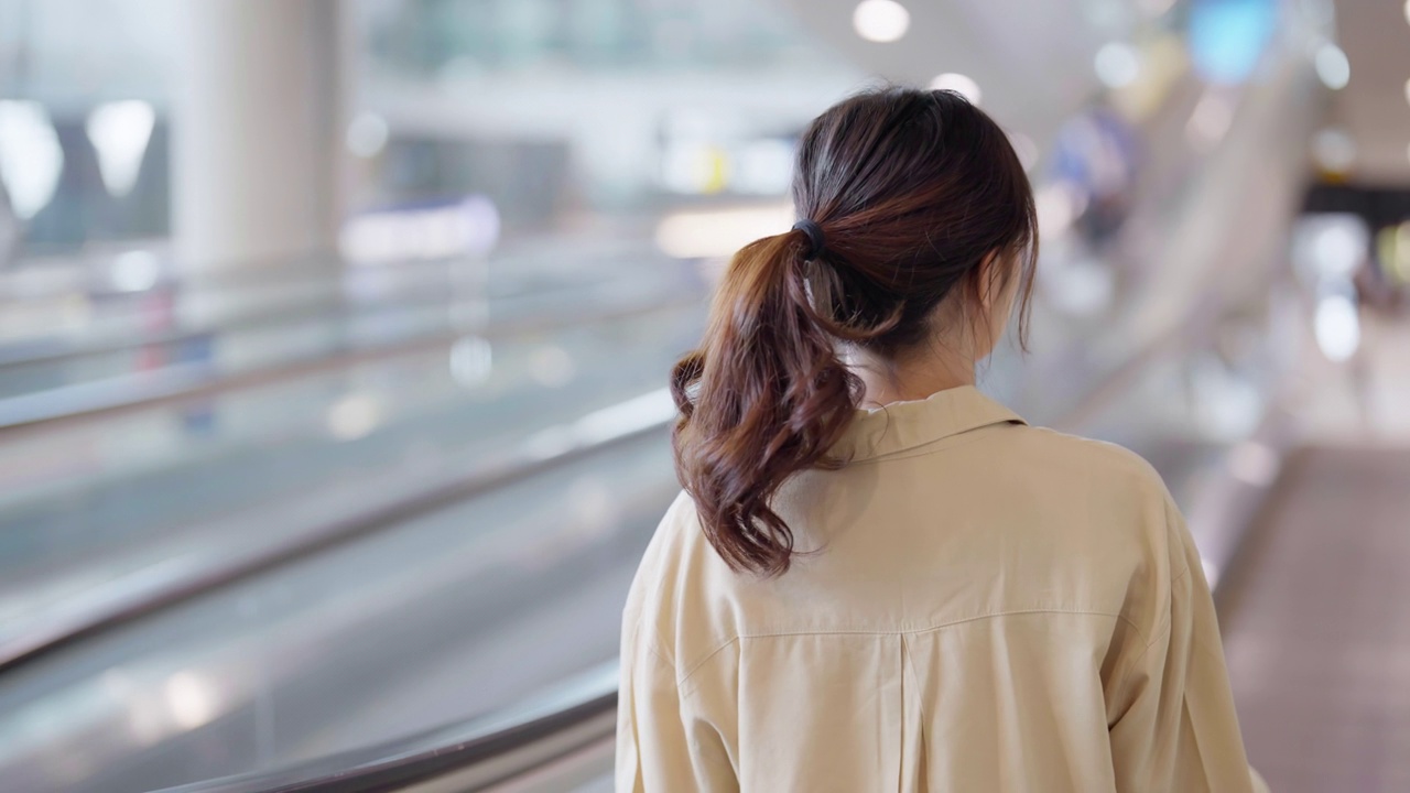 年轻的亚洲女乘客在机场候机楼或现代火车站。亚洲女性通勤者带着行李乘坐自动扶梯视频素材