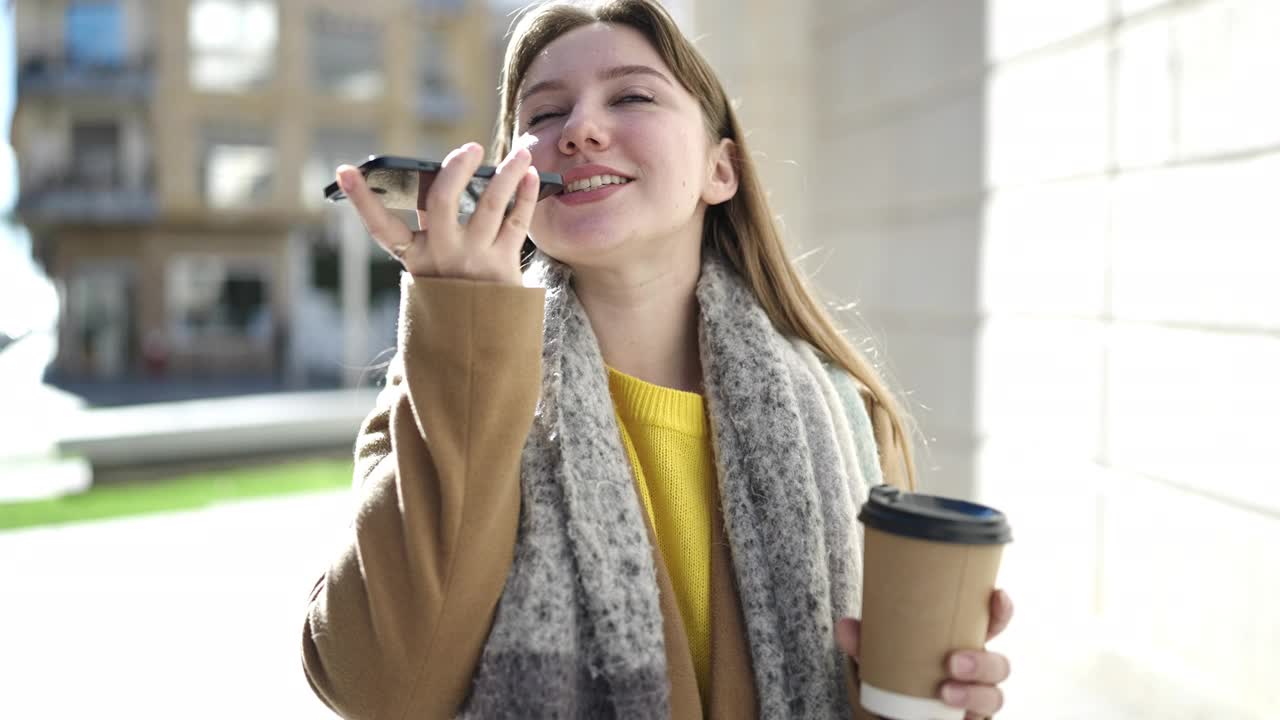 年轻的金发女子在街上用智能手机聊天，喝咖啡视频素材