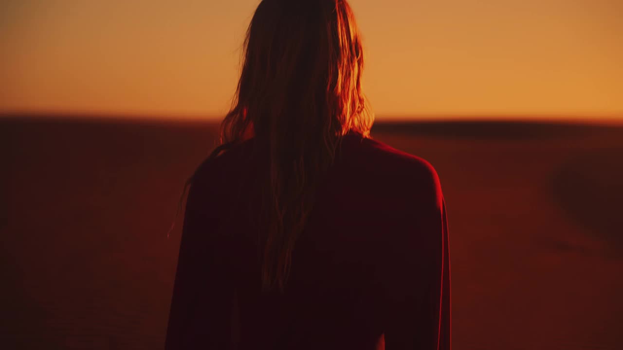 夕阳下，沿着阳光明媚的沙丘散步的女人的剪影视频素材