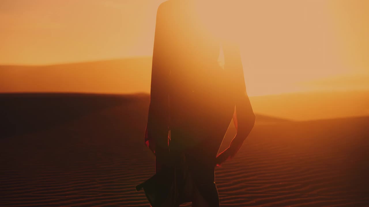 夕阳下，沿着阳光明媚的沙丘散步的女人的剪影视频素材