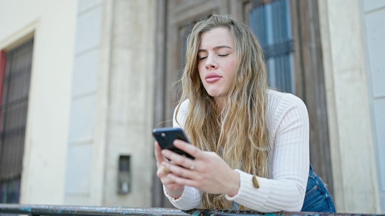 年轻的金发女子在街上用着智能手机，表情严肃视频素材