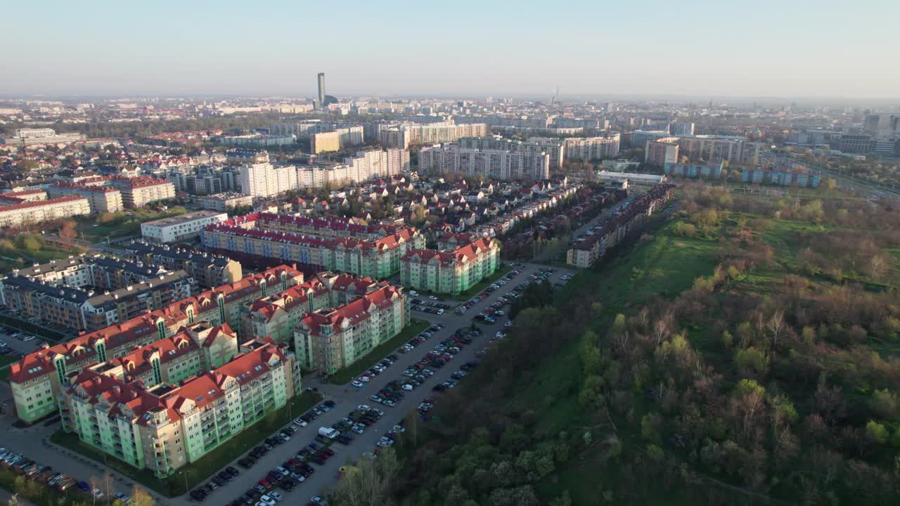 一架无人机拍摄的鸟瞰图，在日出时飞过一座城市的住宅。房屋之间有大量的绿色植物，道路和停放的汽车清晰可见，而城市仍在沉睡。视频素材